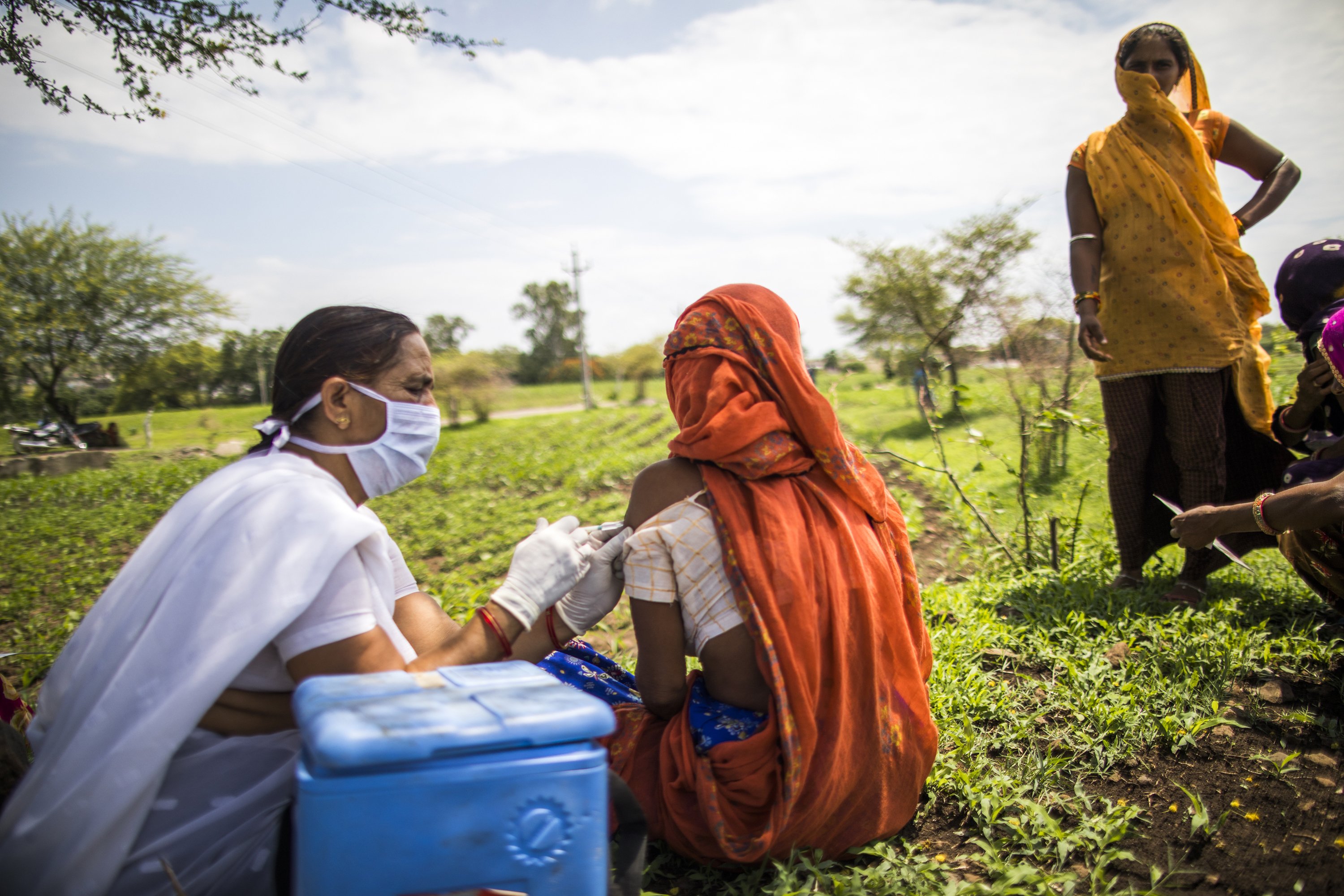 A woman receives a dose of COVID-19 vaccination as a female health worker conducts a vaccination session in an open field outside a community health center in Banswada, India.