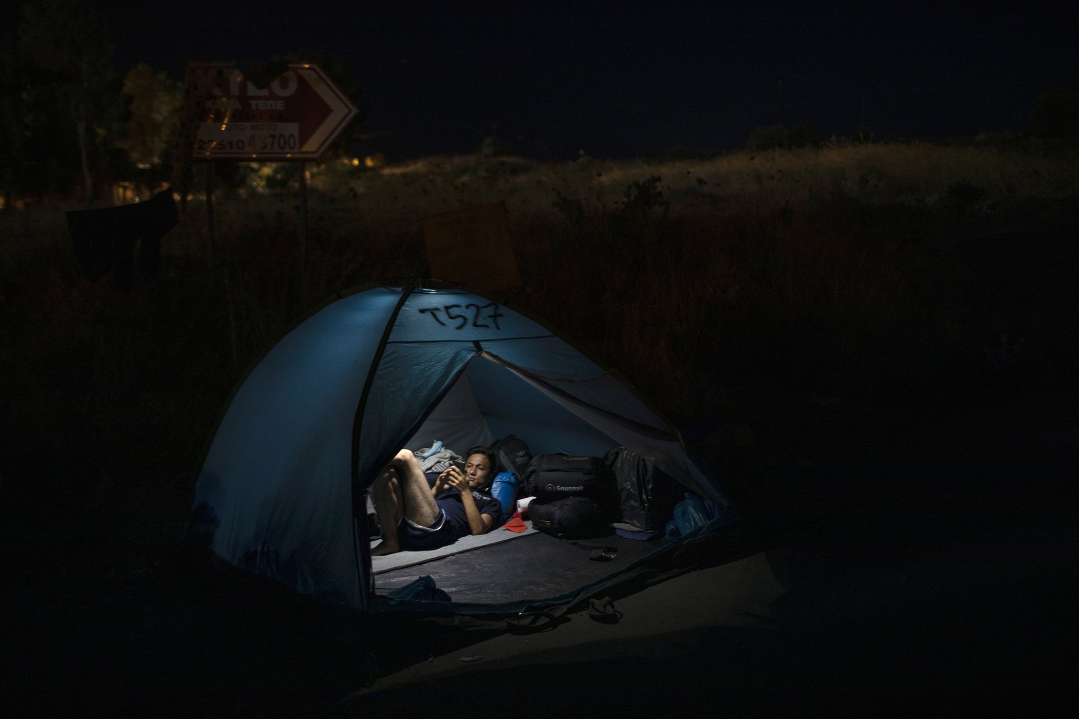 An Afghan man from the destroyed Moria camp, looks at he mobile phone as he rests in a tent, on the road that refugees and migrants are sheltered on, in Lesbos island, Greece, Sept. 17, 2020.
