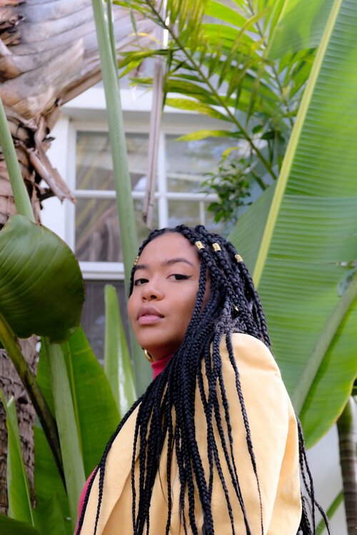 Activist Niki Franco looks over her shoulder towards the camera, surrounded by greenery.