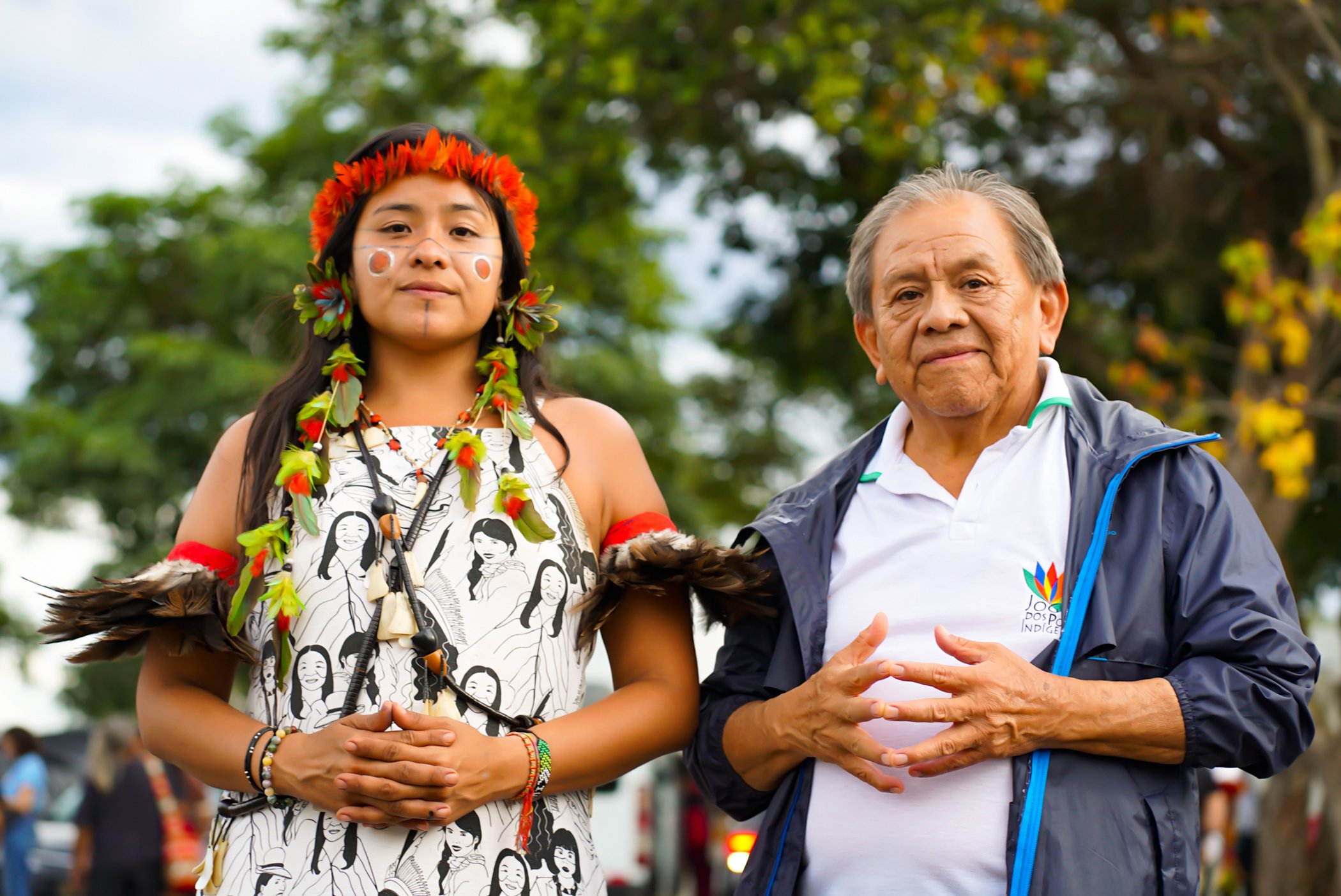 An older Brazilian man stands behind a younger woman, father and daughter Taily and Marcos Terena, with their hands clasped in front of them as they look directly at the camera.