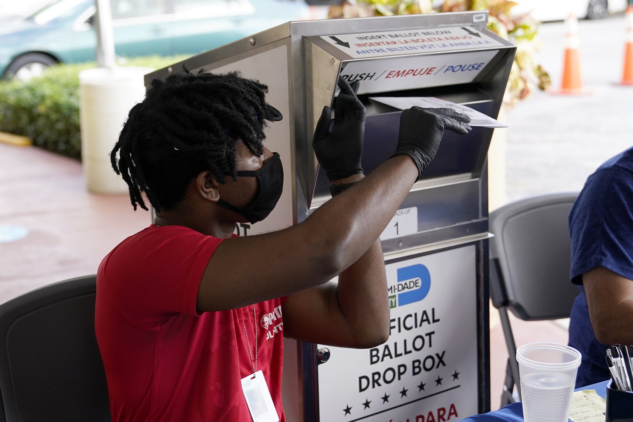 Election worker Najeh Fisher places a vote-by-mail ballot for the Nov. 3 general election into an official ballot drop box at the Miami-Dade County Elections Department, Oct. 14, 2020, in Doral, Fla.