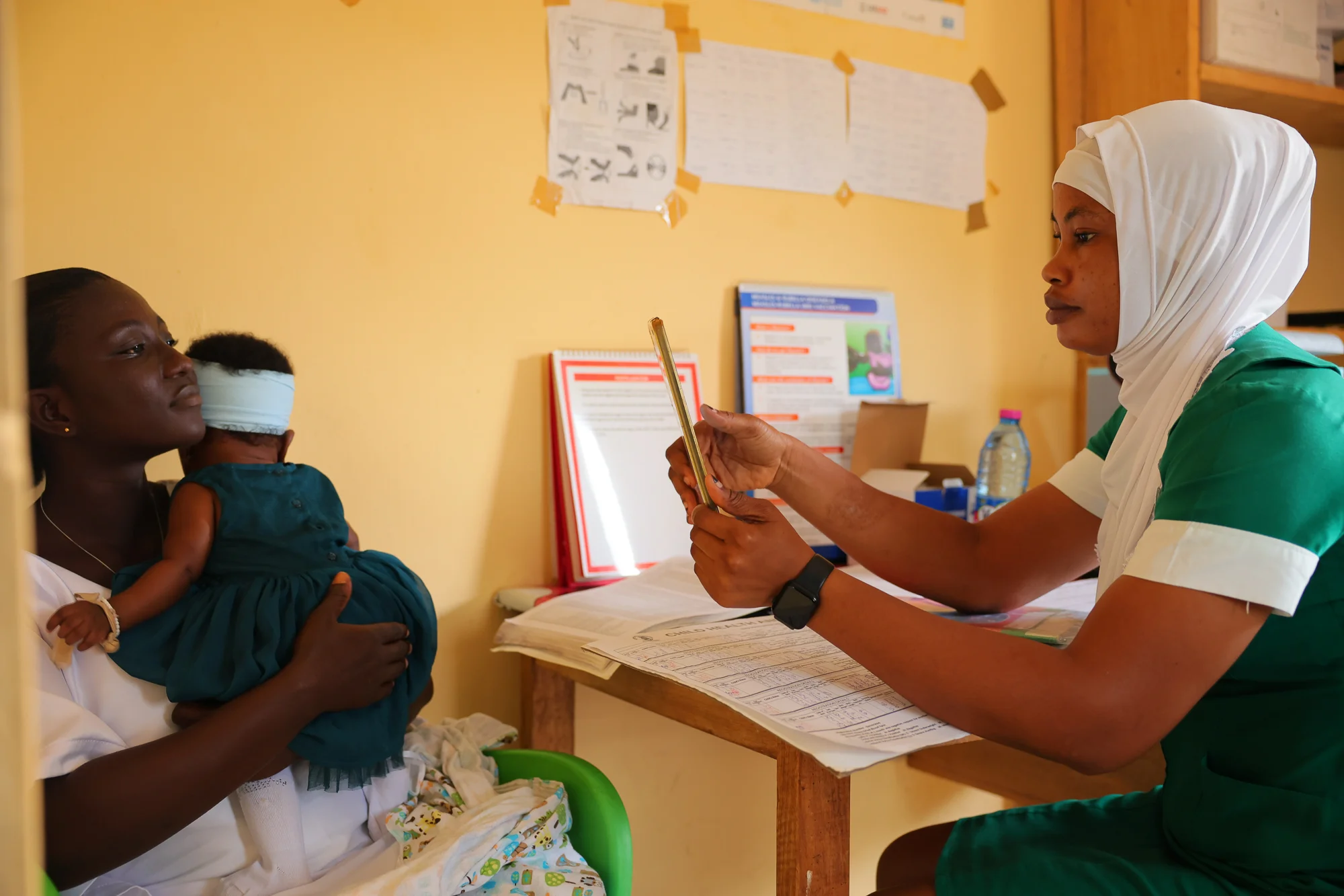 Zainab Abdulahi (R), 29, a community health nurse, verifies the identity of Abigail Debrah (L), 24, using the Simprints biometric system at the Kotokuom CHPS Compound, Ayemansa District, Eastern Region, Ghana, on July 16, 2025.