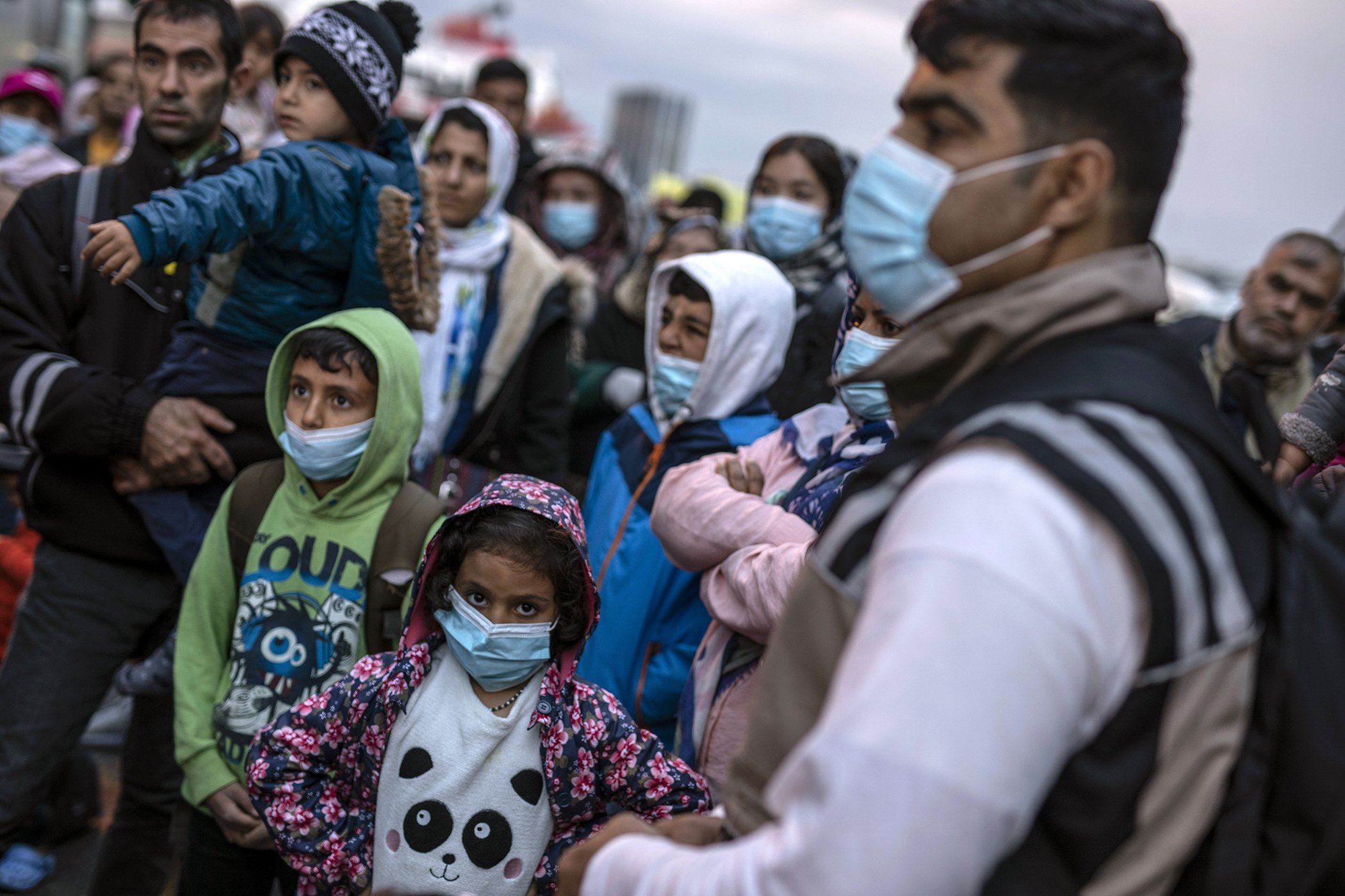 Refugees and migrants wearing masks wait to get on a bus after their arrival at the port of Piraeus on May 4, 2020. Greek authorities are moving 400 migrants to the mainland to help ease overcrowded conditions at the camp Moria in Lesbos island.