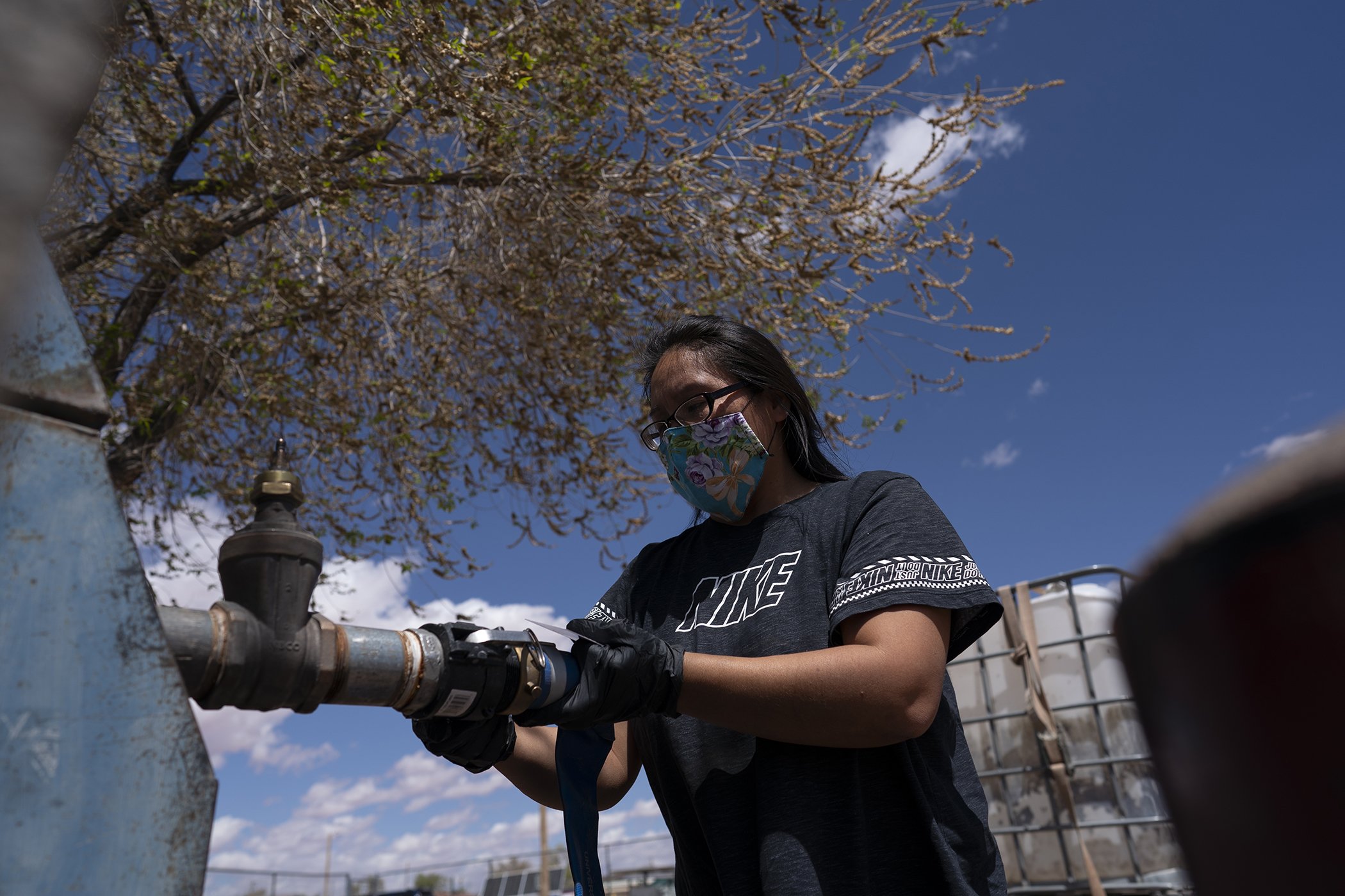 Raynelle Hoskie attaches a hose to a water pump to fill tanks in her truck outside a tribal office on the Navajo reservation in Tuba City, Ariz., on April 20, 2020. Hoskie is hauling water back to her home where she lives with her extended family.