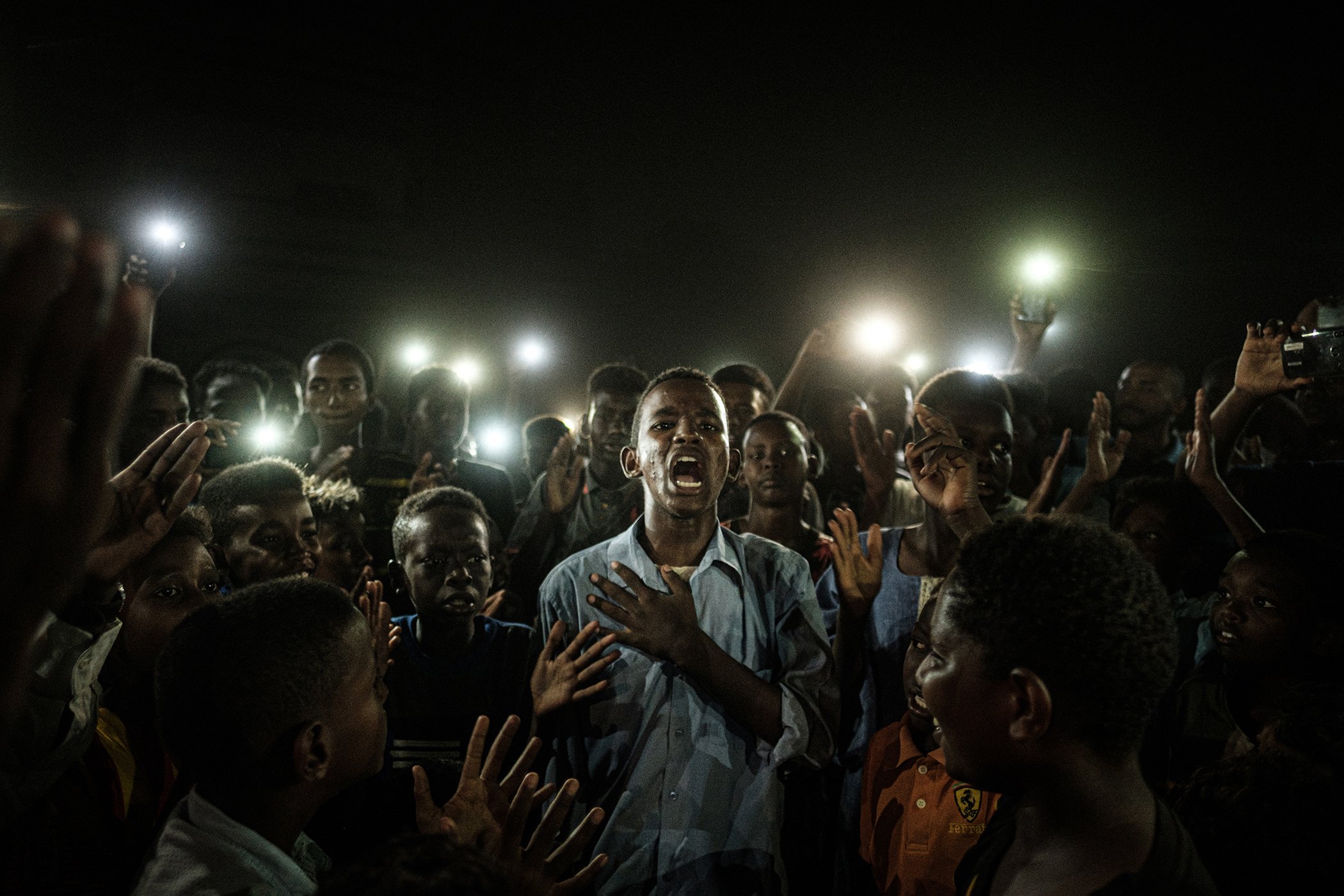 A young man, illuminated by mobile phones during a blackout, recites protest poetry while demonstrators chant slogans calling for civilian rule, in Khartoum, Sudan, on June 19, 2019.