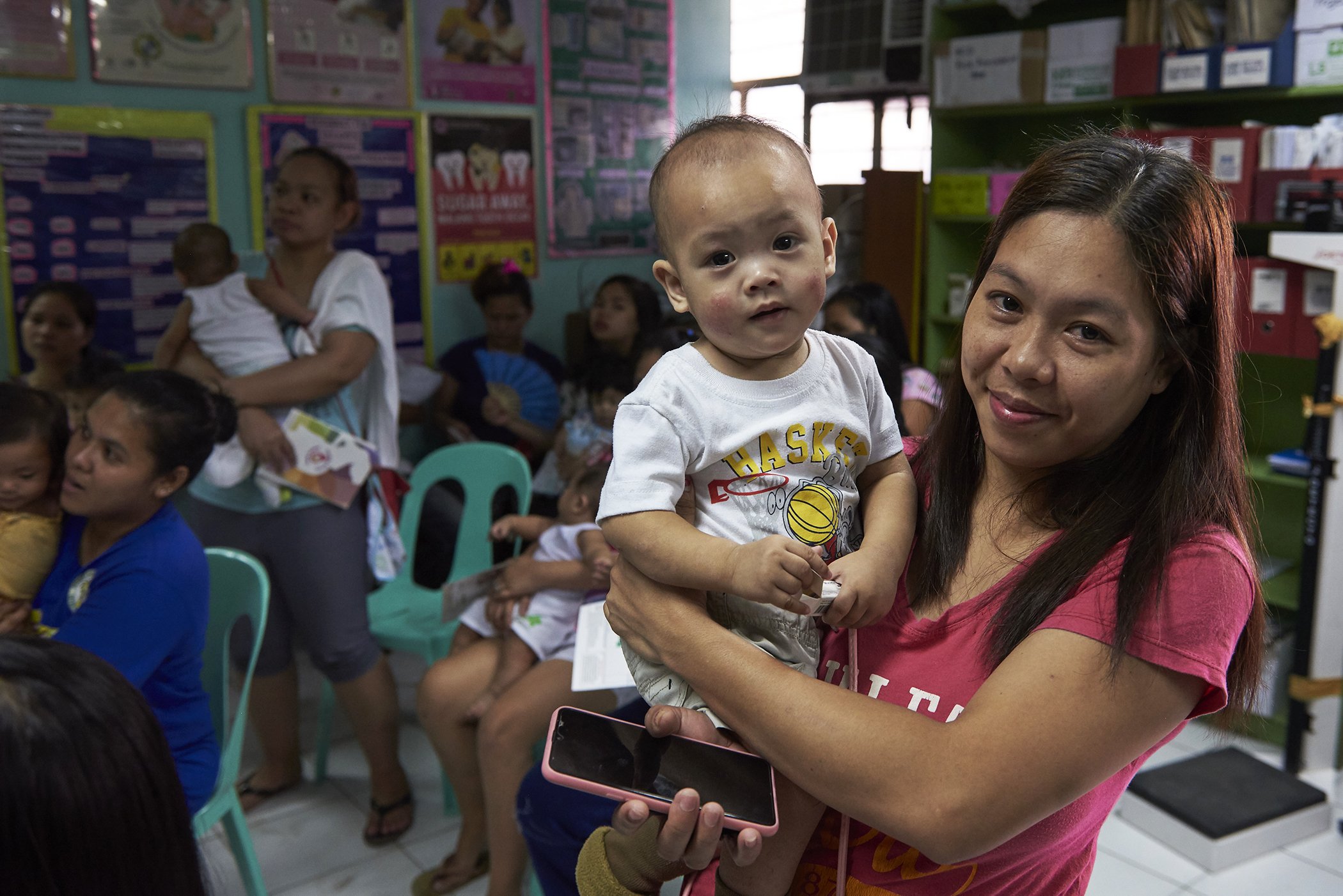 Gennie Oliva stands holding her child Kivet Marten-Oliva after receiving a vaccination for the child against measles, mumps, and rubella (MMR) at Lower Bicutan Health Centre in Taguig City, Philippines, on March 26, 2019.