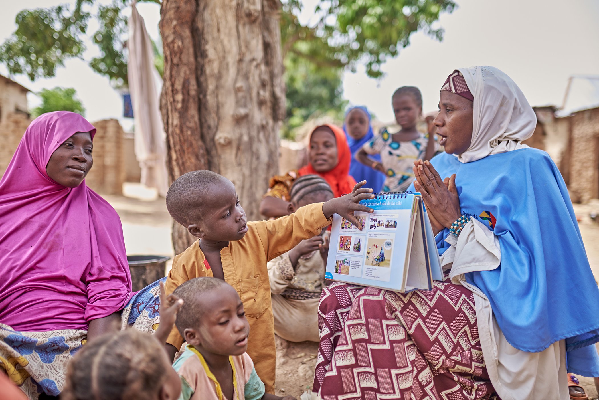A young child looks at the educational materials brought by Furera Aliyu as she speaks to women in the community on immunization, antenatal care, and general health in Nigeria's Bauchi state in October 2023.