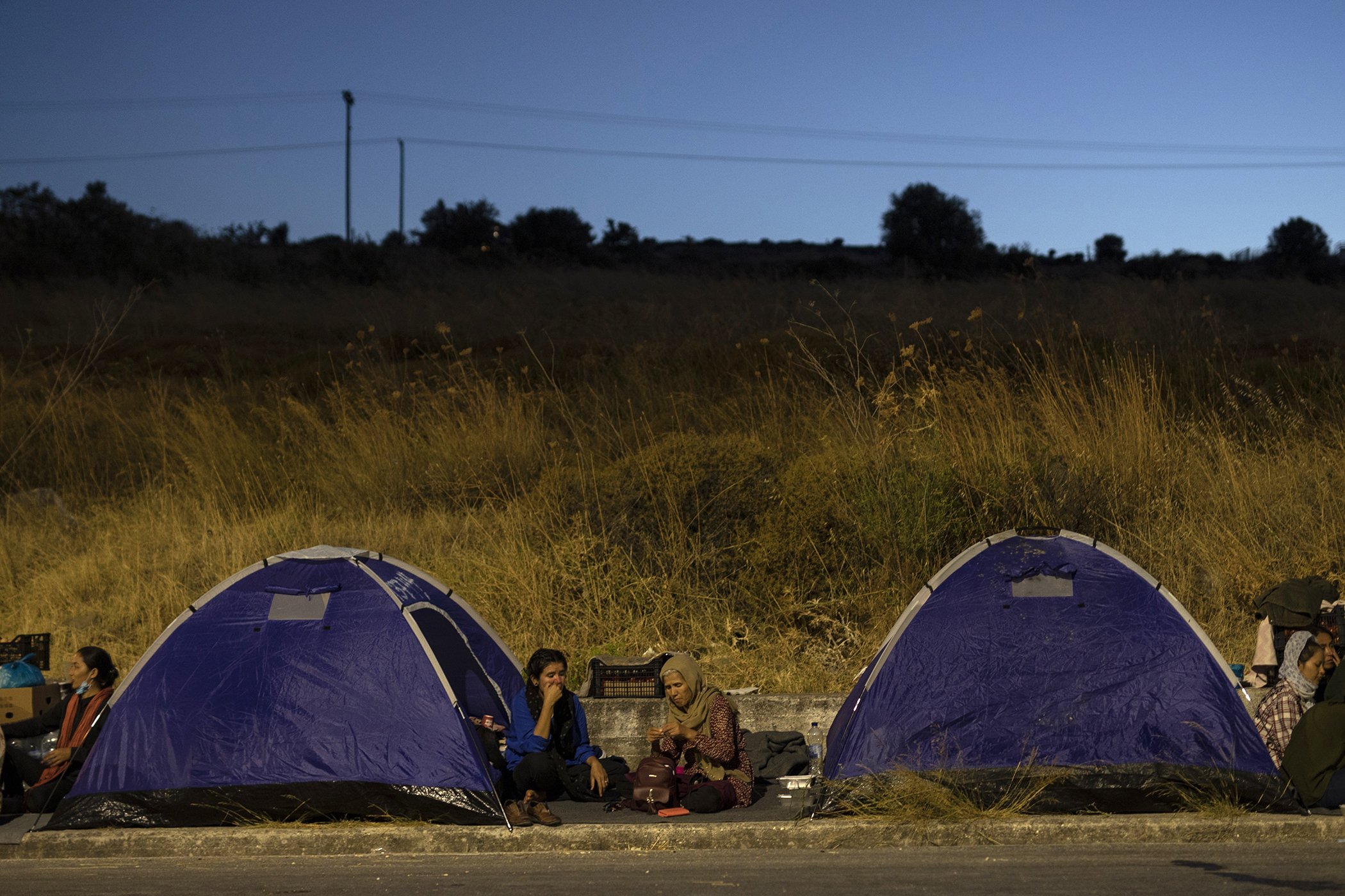 Migrants sit outside their tents as they gather on the roadside on the northeastern island of Lesbos, Greece, Sept. 10, 2020. Little remained of Greece's overcrowded Moria refugee camp Thursday after a second fire overnight destroyed nearly everything.