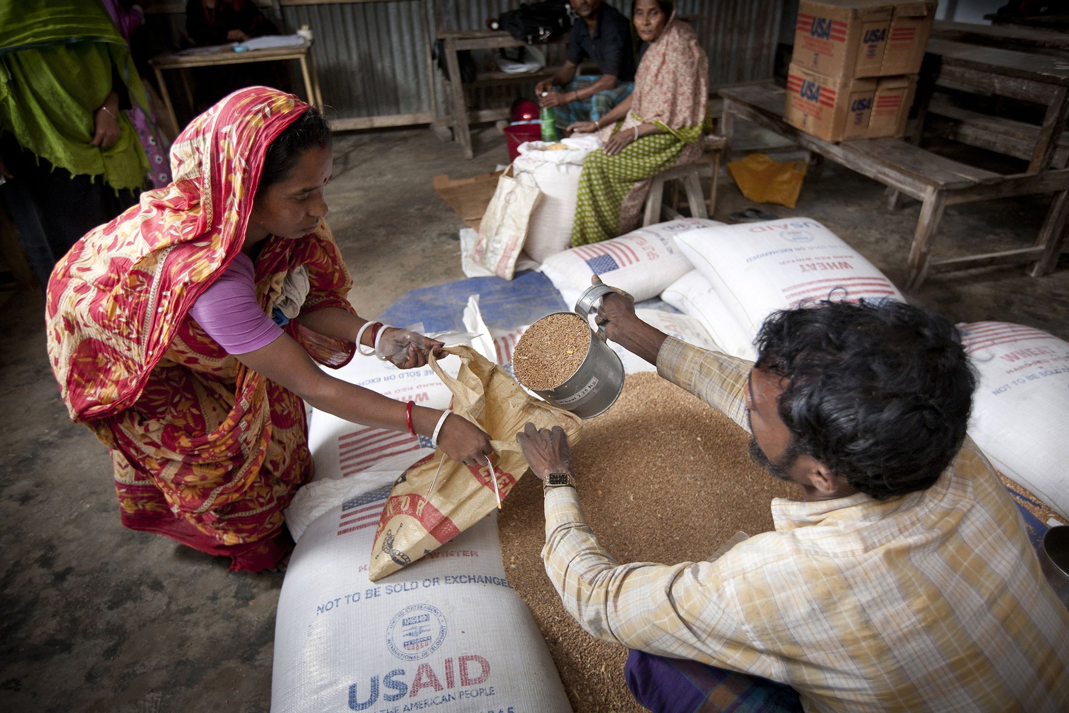 A woman takes wheat, yellow peas and oil during a food distribution service organized by Save the Children and its partner CODEC in Barisal District, Bangladesh.