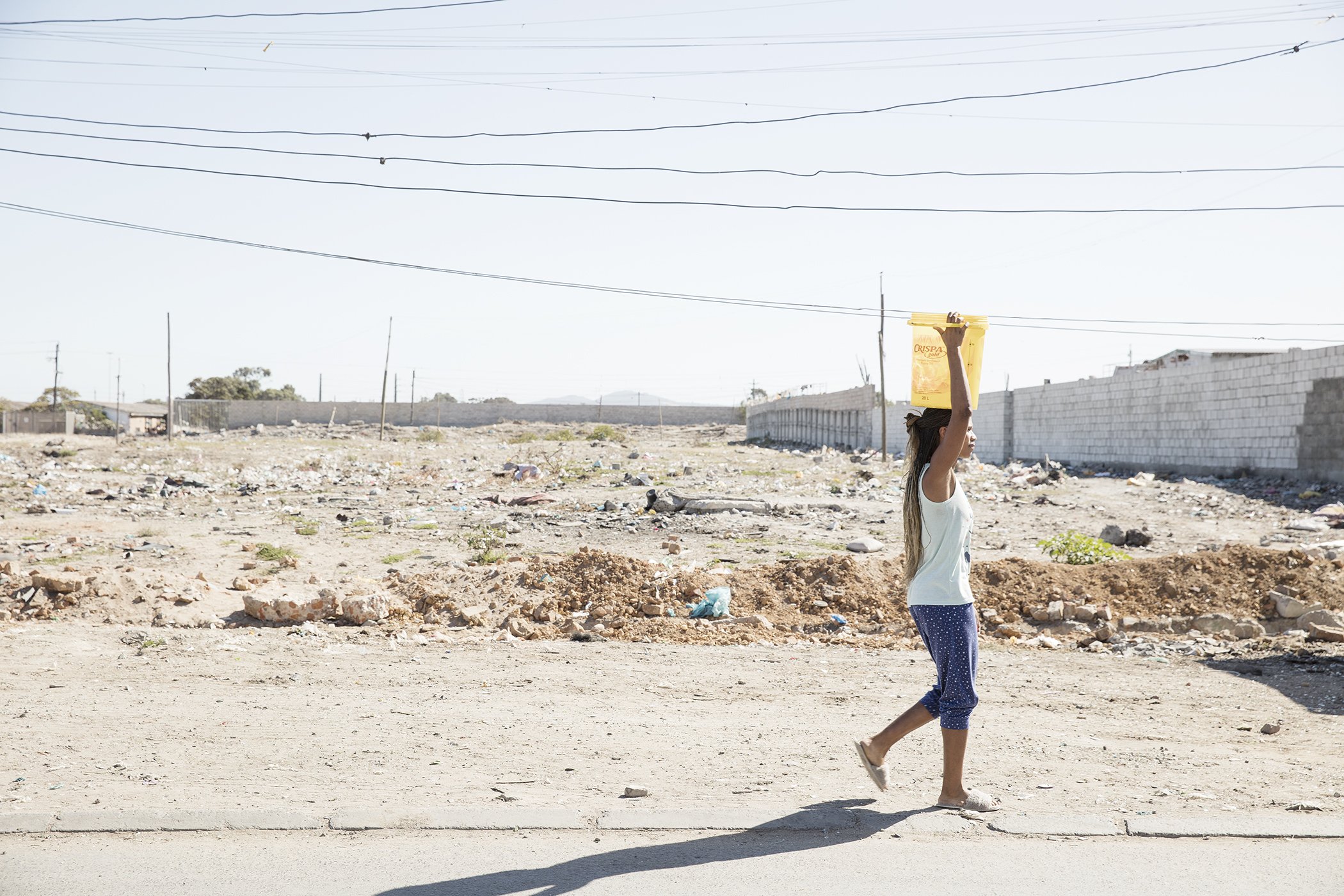 A young woman carries water back to her home within the township of Phillipi.