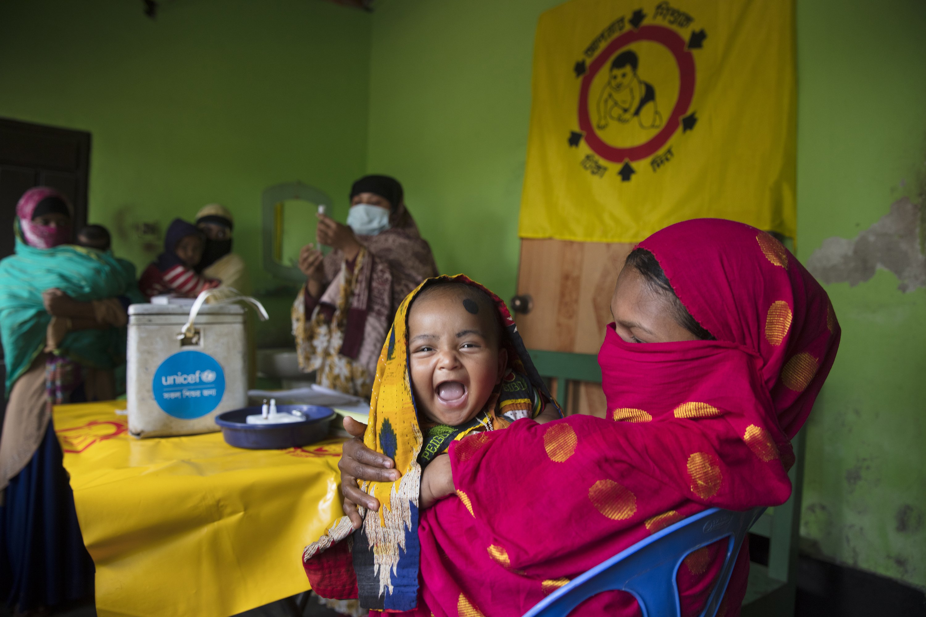 A child smiles as she sits on her mother’s lap before receiving a vaccination in an outreach EPI Center on Jan. 25, 2021 at Trishal, Mymensingh, Bangladesh.