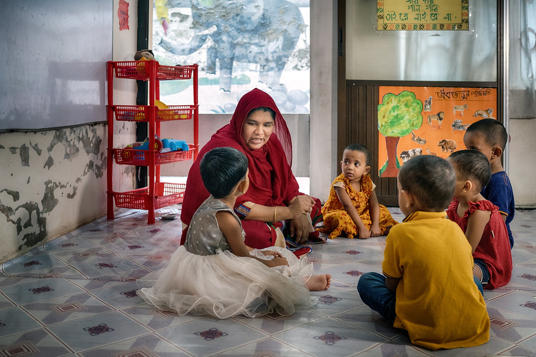 Nazmin, one of the caregivers at the child care center in Evince Garments Limited, sits with kids for a lesson.