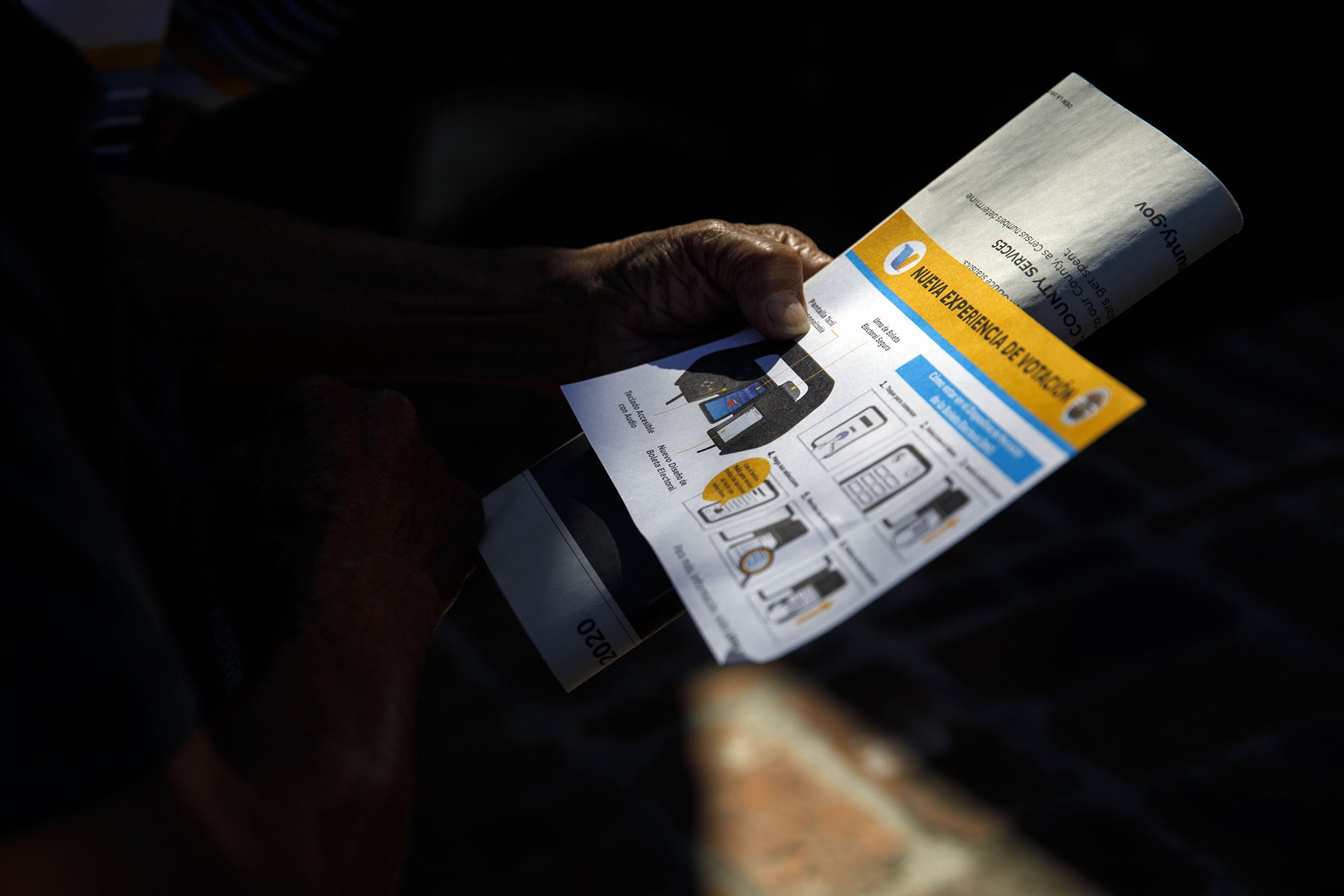 A voter reads about voting changes in Spanish while waiting in line to enter a polling station in the Echo Park Recreation Complex in Los Angeles, Calif., March 3, 2020.