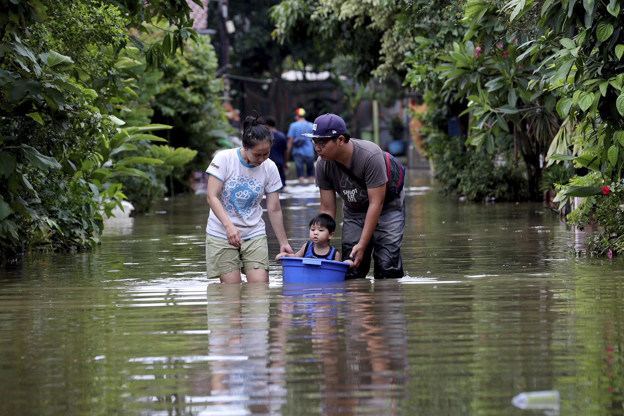 A family walks their son through a flooded neighborhood in a bucket in Tanggerang on the outskirts of Jakarta, Indonesia, Jan. 2, 2020.