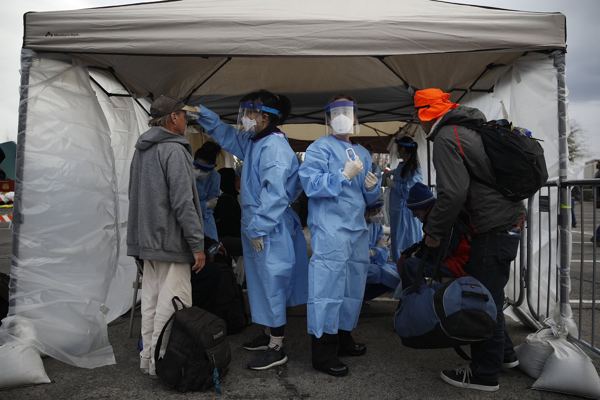 Medical students Claire Chen, center left, and Miranda Stiewig, center right, take people's temperatures to screen for possible coronavirus cases at a makeshift camp for the homeless, March 28, 2020, in Las Vegas, NV.