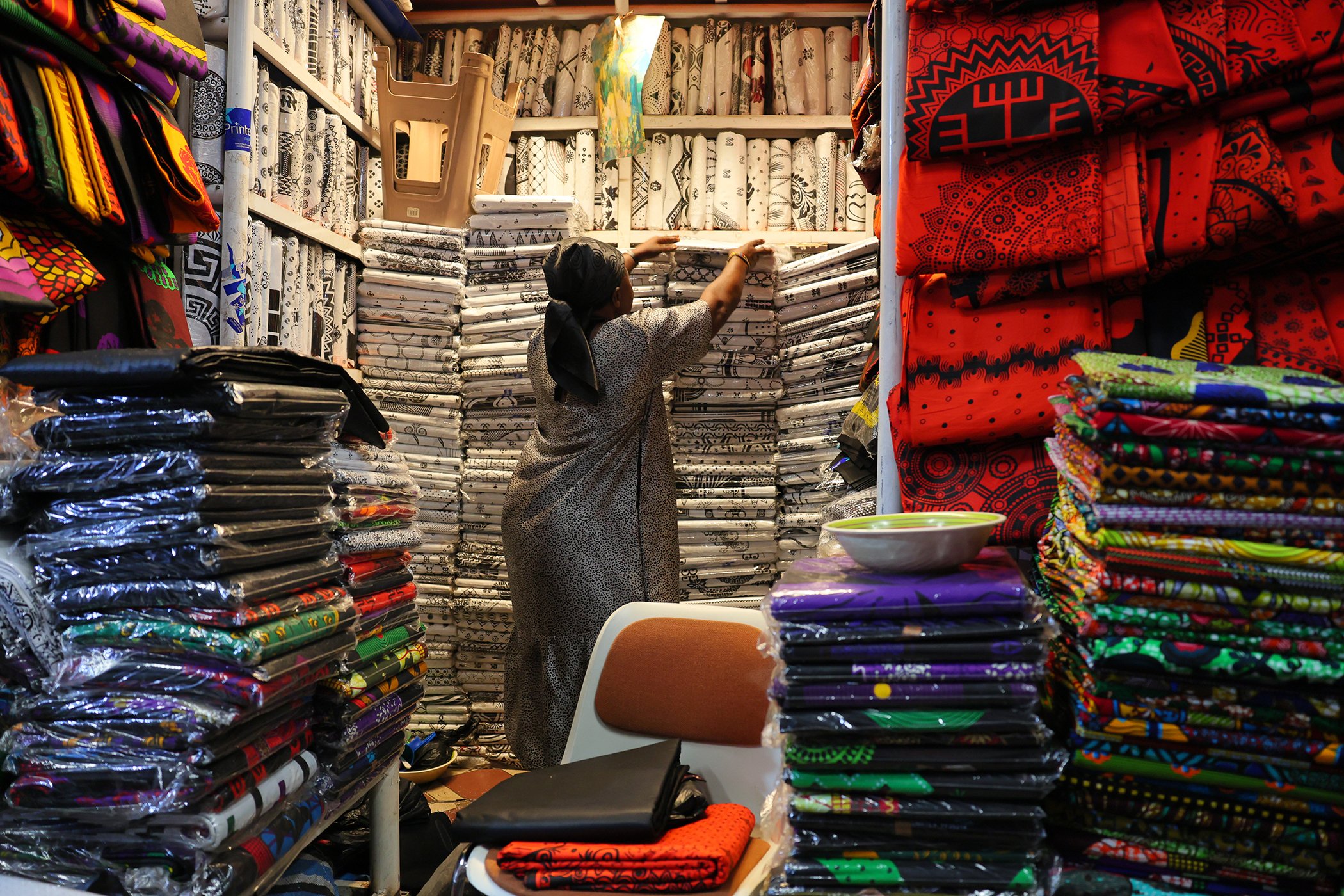 A vendor arranges piles of brightly dyed, locally made fabrics at the bustling Kejetia Market in Kumasi, Ghana, August 5, 2025.