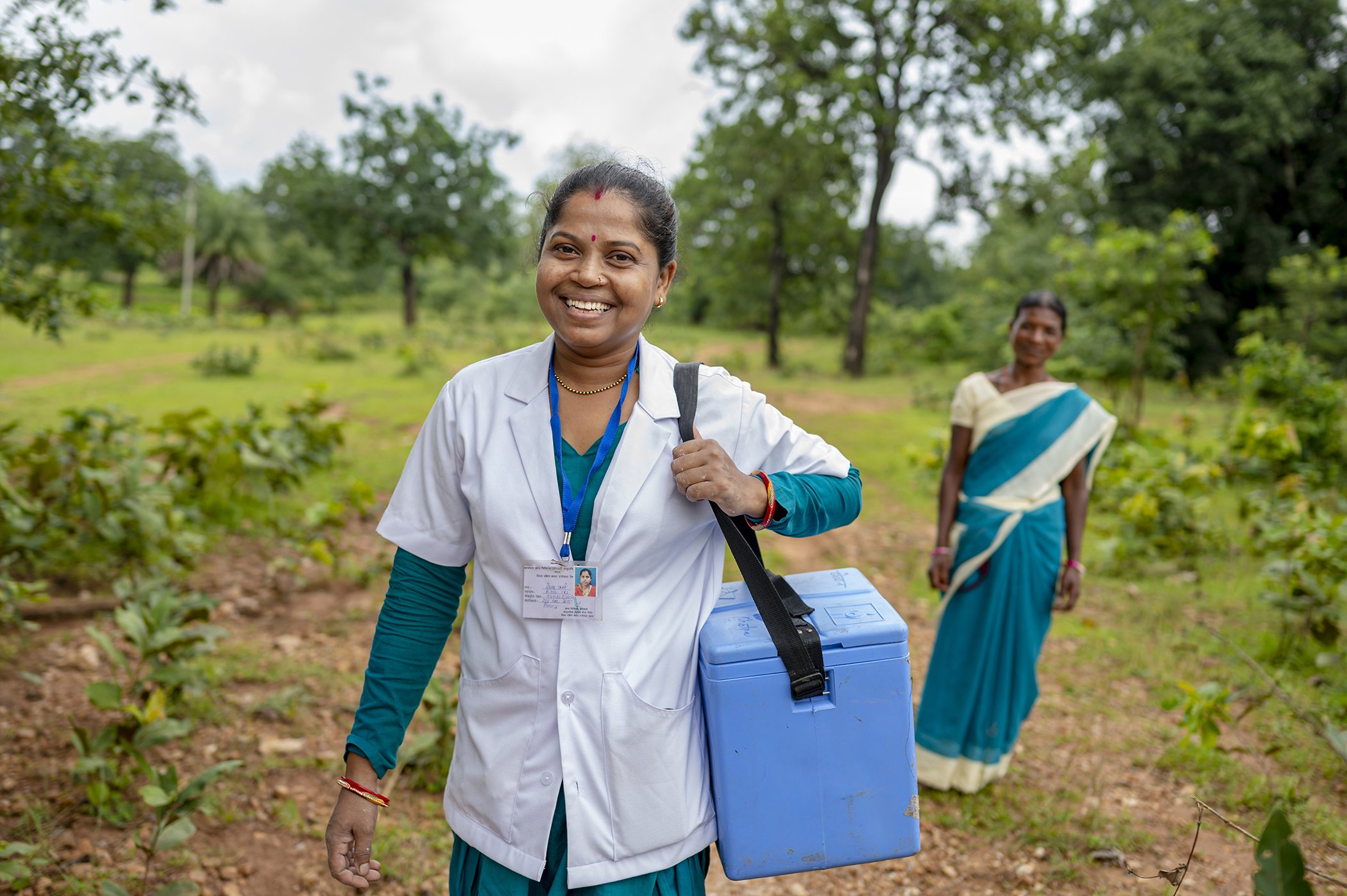 Health care workers carry vaccines through difficult terrain as part of a village health, sanitation, and nutrition day in the Chhattisgarh State, India in August 2021.