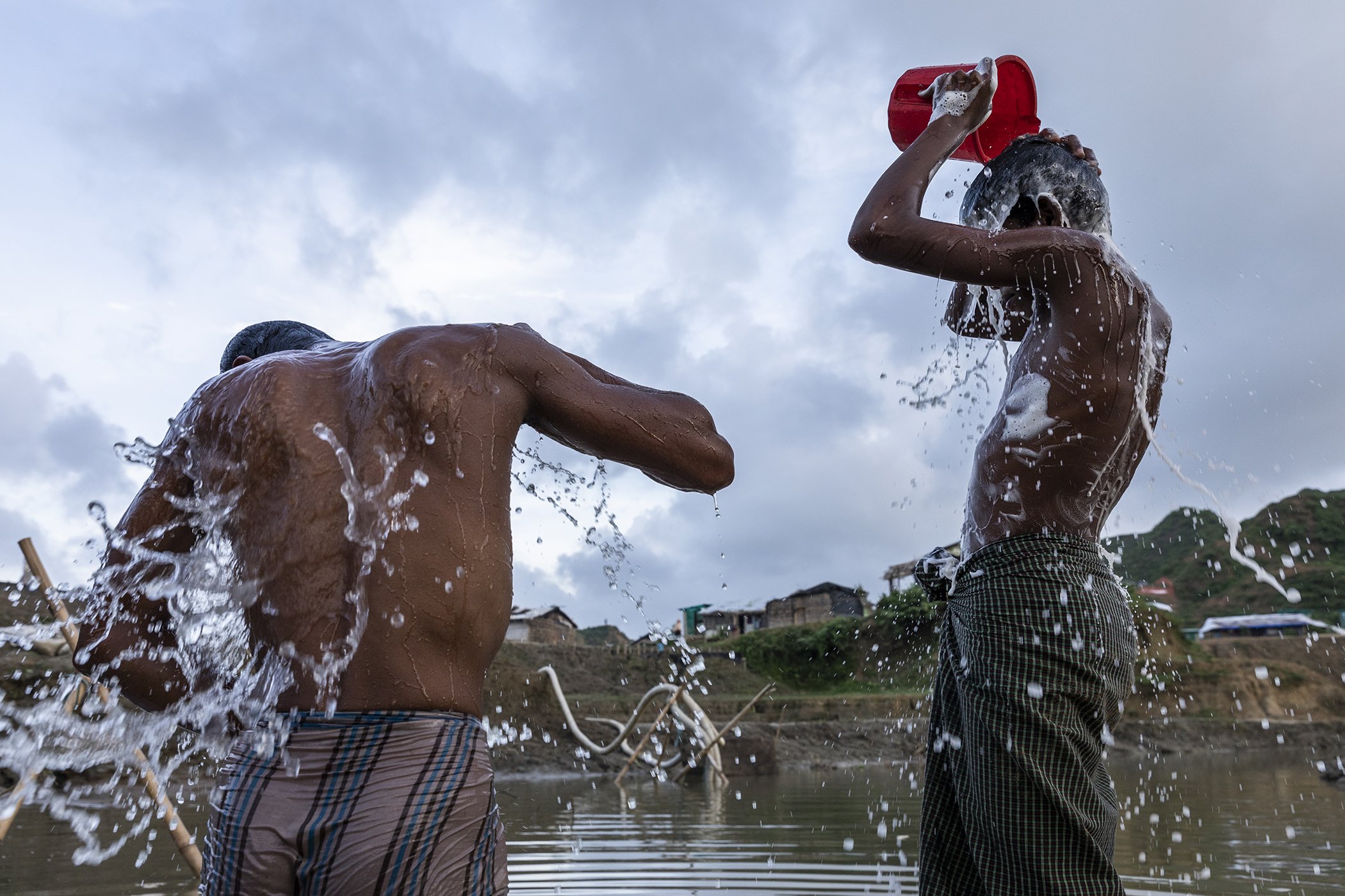 Two young men bathe in Nayapara refugee camp, Cox's Bazar, Bangladesh in July 2018. The Boro Chara stream’s heavy brown sediment water is treated to remove sediment, and chlorine is added to make it safe to drink.