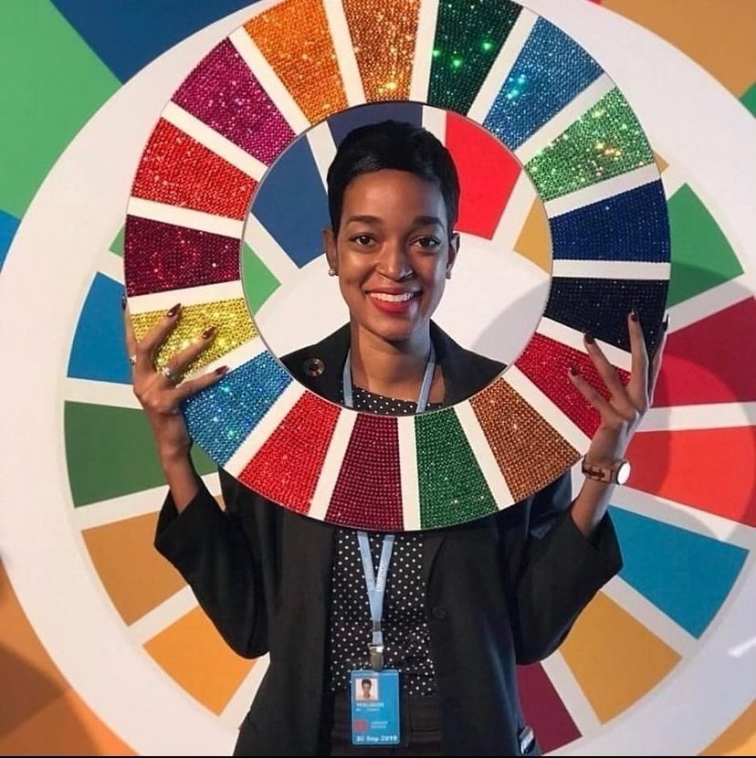Jhannel Tomlinson smiles while holding a sparkly circle representing the United Nations' Global Goals.