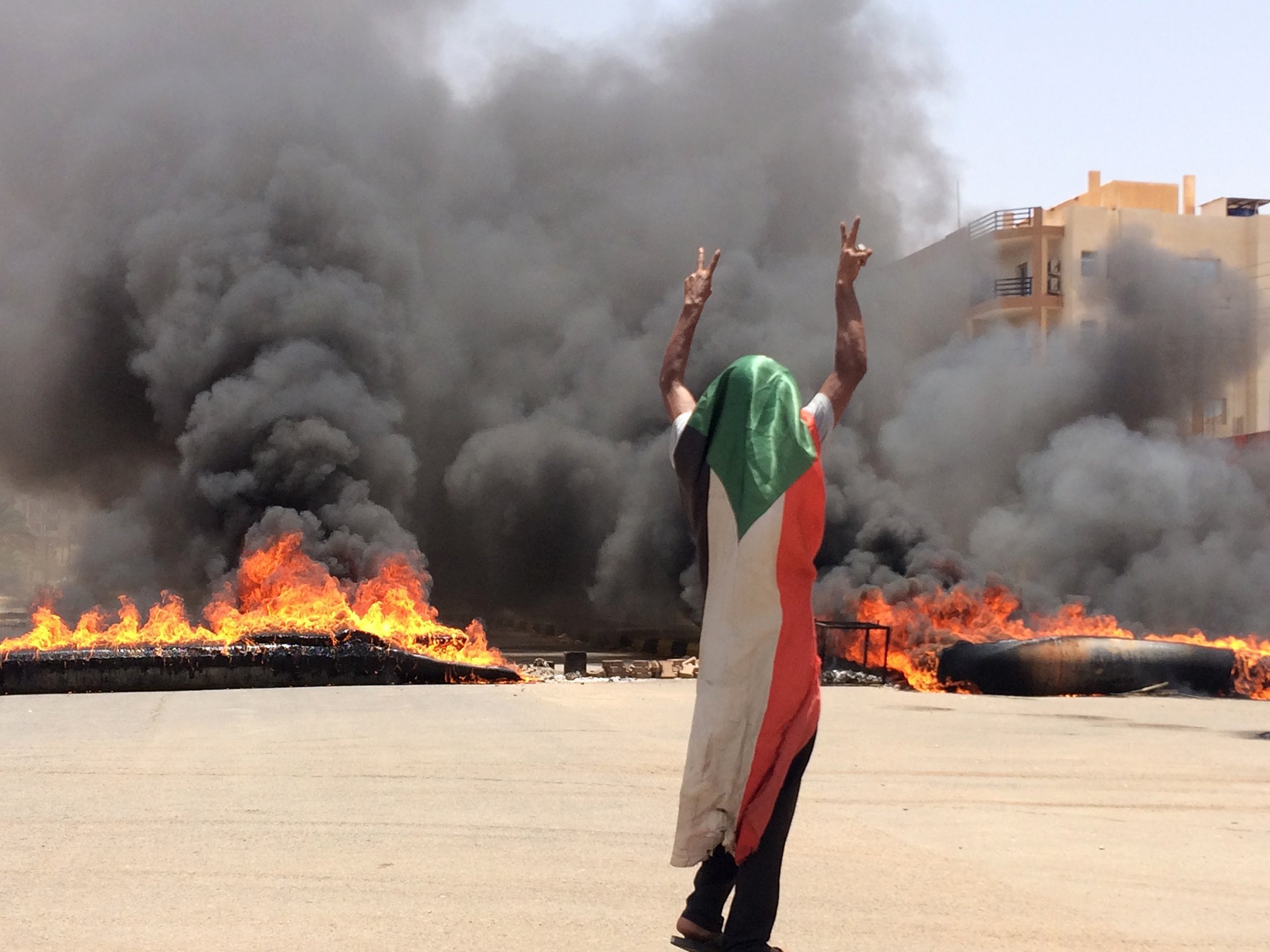 A protester wearing a Sudanese flag flashes the victory sign in front of burning tires and debris on the road, near Khartoum's army headquarters, in Khartoum, Sudan, June 3, 2019.