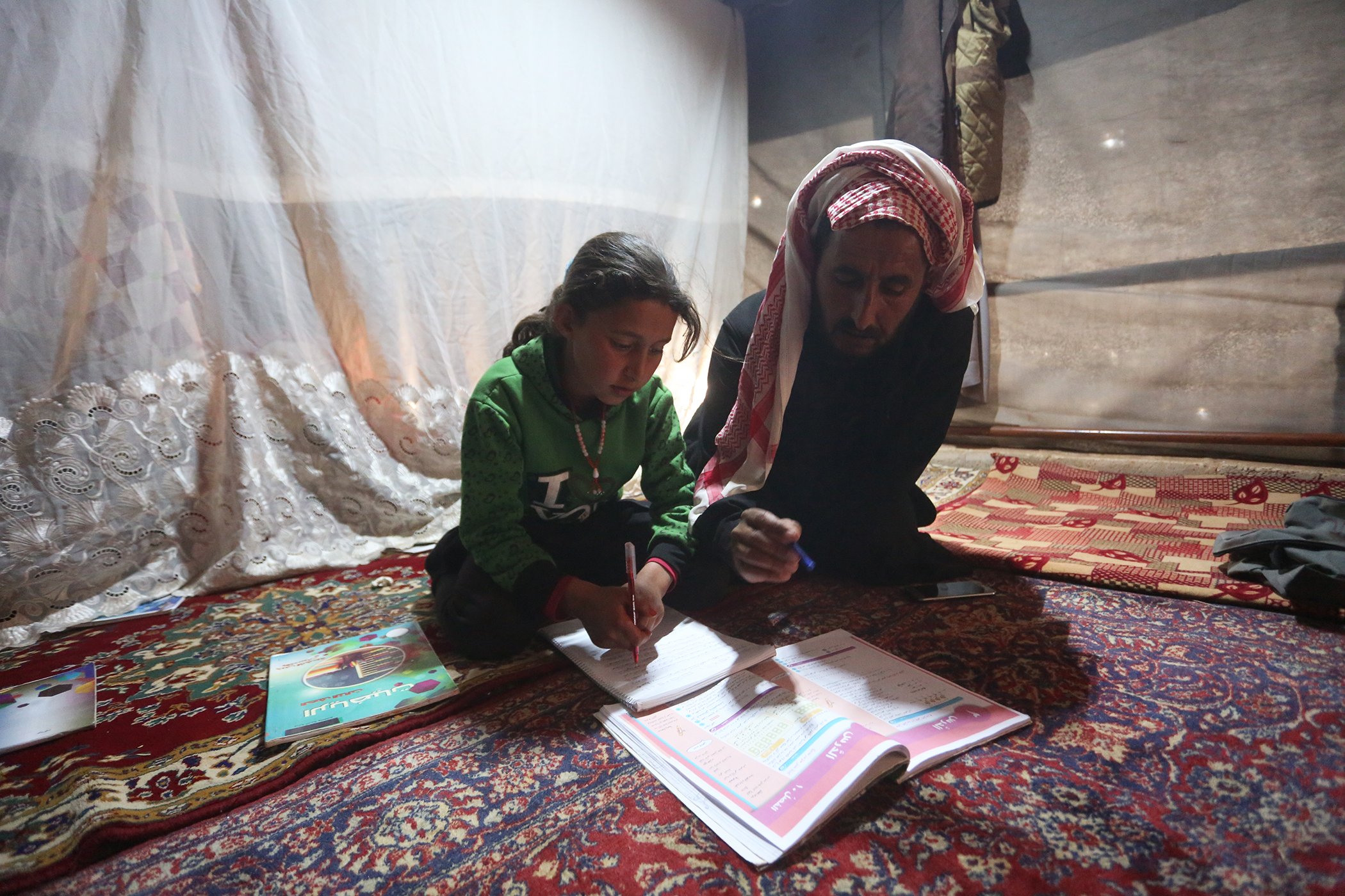 Maria, 9, and her father follow a pre-recorded lesson on her father’s smartphone in a tent at the Kili IDP camp in rural Idlib, Syrian Arab Republic in April 2020.