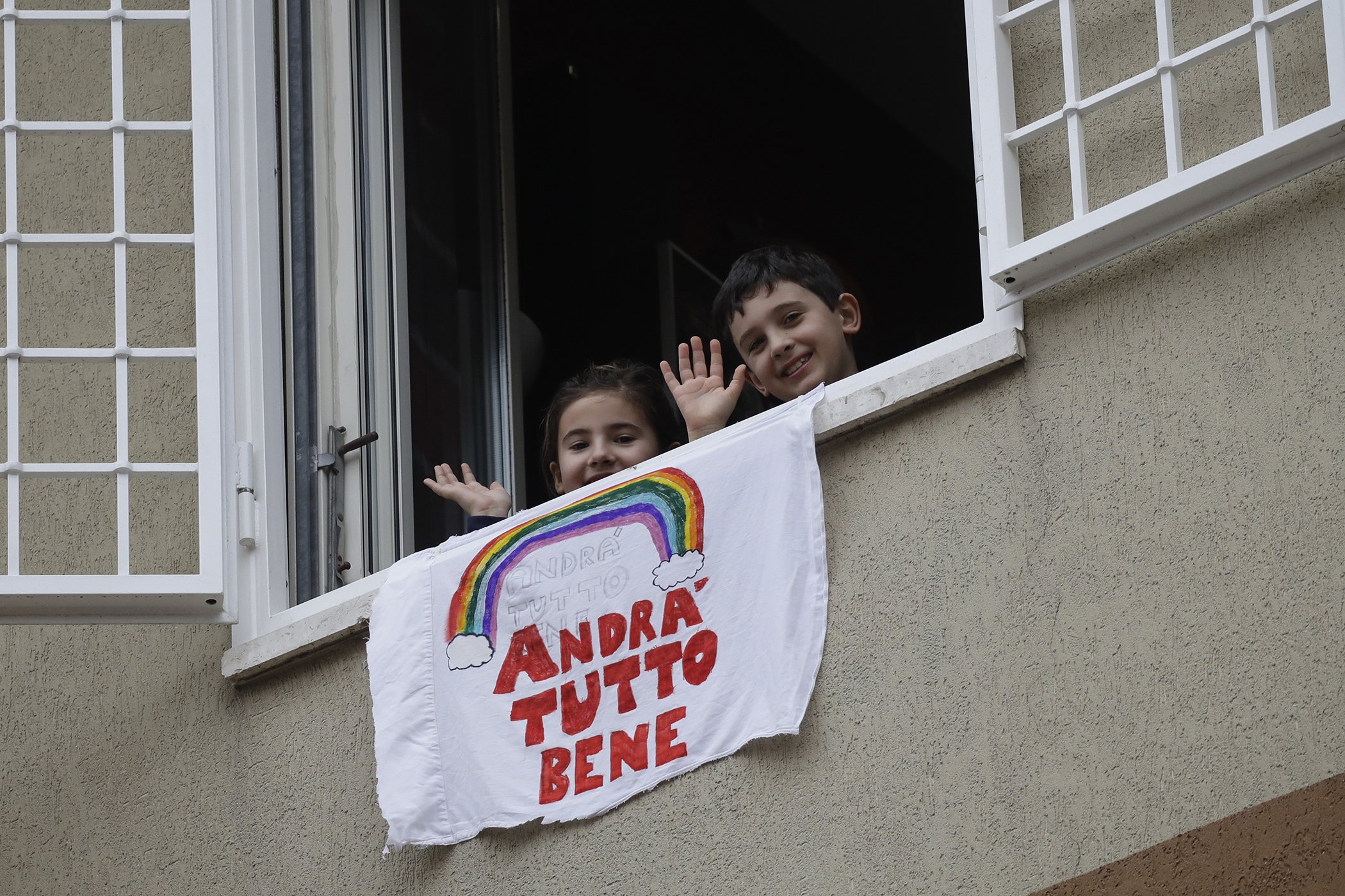 Francesco and Greta Innominati wave after placing a banner reading "Everything is gone be all right" out of a window of their apartment in Rome on March 13, 2020. Children’s drawings of rainbows are appearing all over social media as well as on balconies.