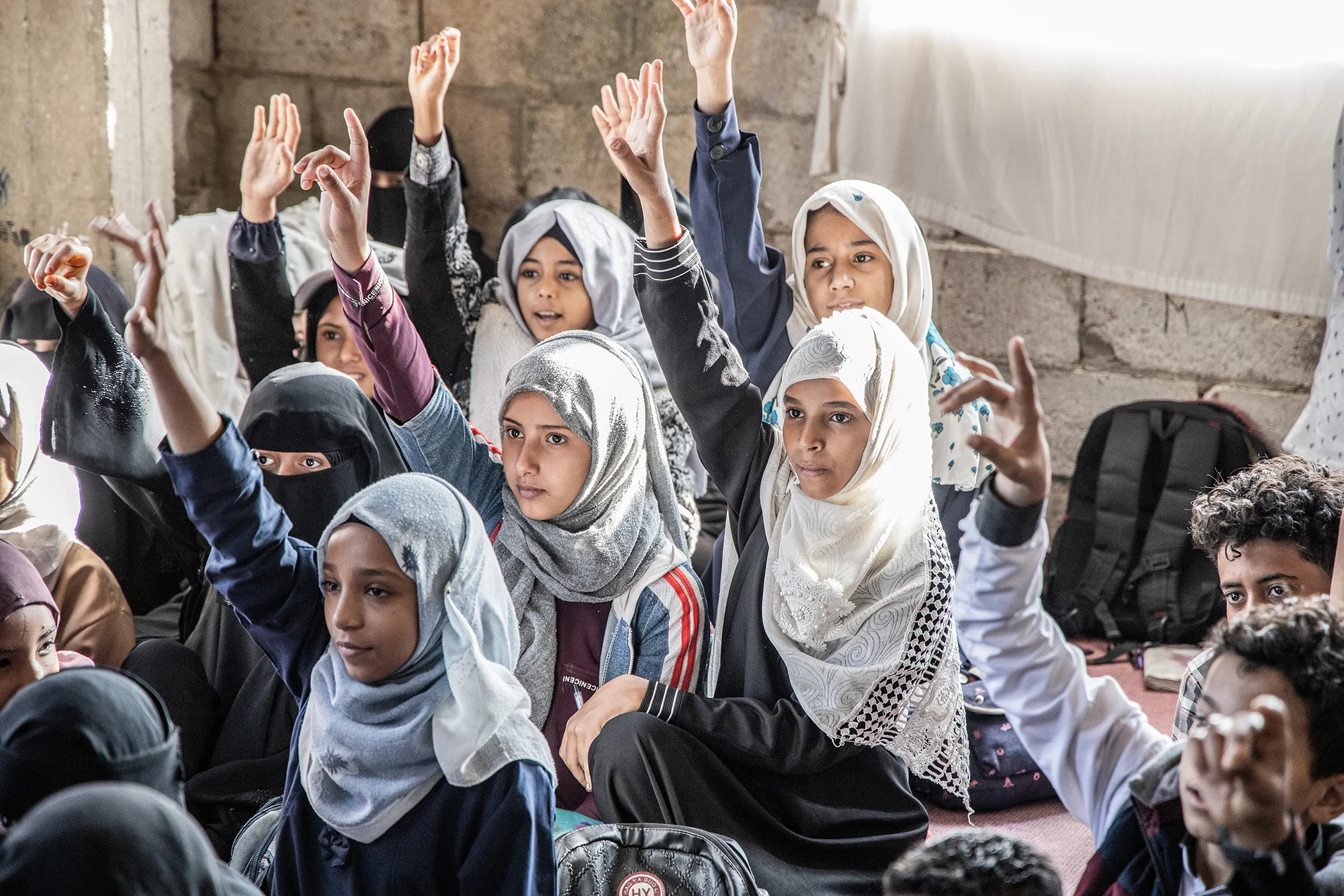 Students raise their hands to answer the teacher's question during class in Taizz, Yemen, 2021. There are many uncertainties and dangers in the building of this school as it's unfinished, with no doors, windows, chairs, and bathrooms.