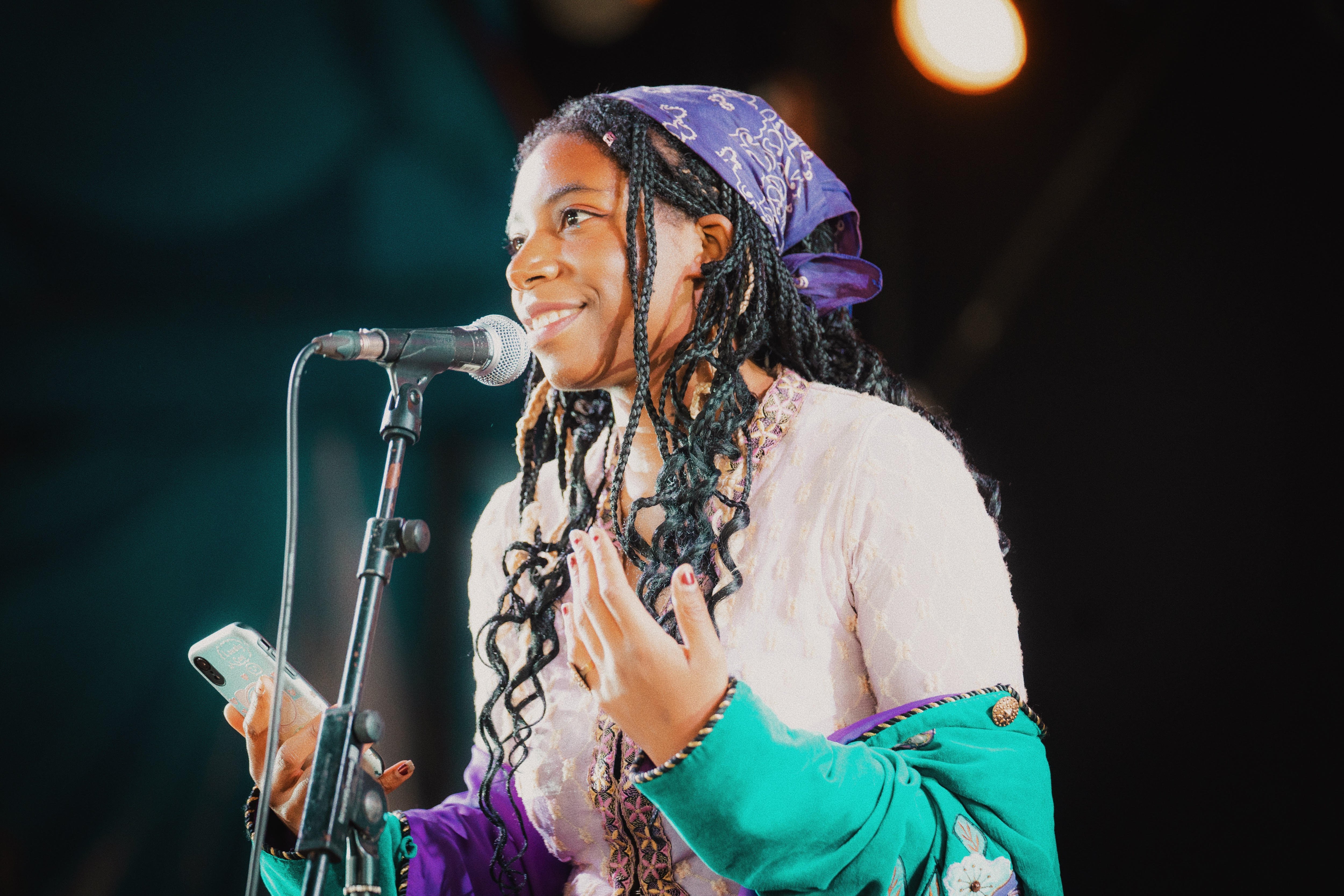 Twenty-two year old climate activist and ecofeminist Dominique Palmer smiles while speaking into a microphone, holding her phone.