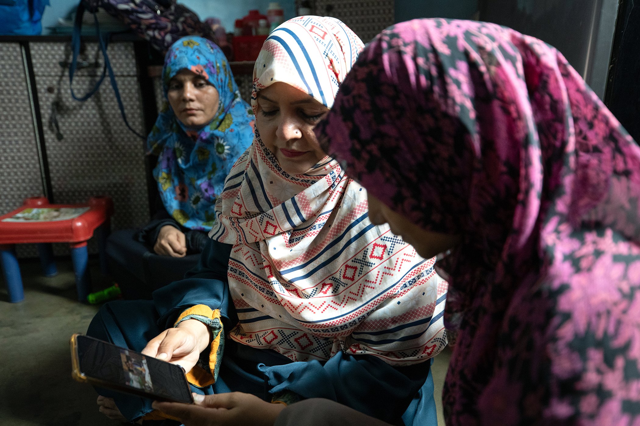 Community Mobilizers, Nusrat Bano (C) and Area In-Charge, Amber Ahmed (L), show San (R) a video of a journalist retracting misinformation he had spread in a previous video that aired on a local news channel in Karachi, Pakistan.