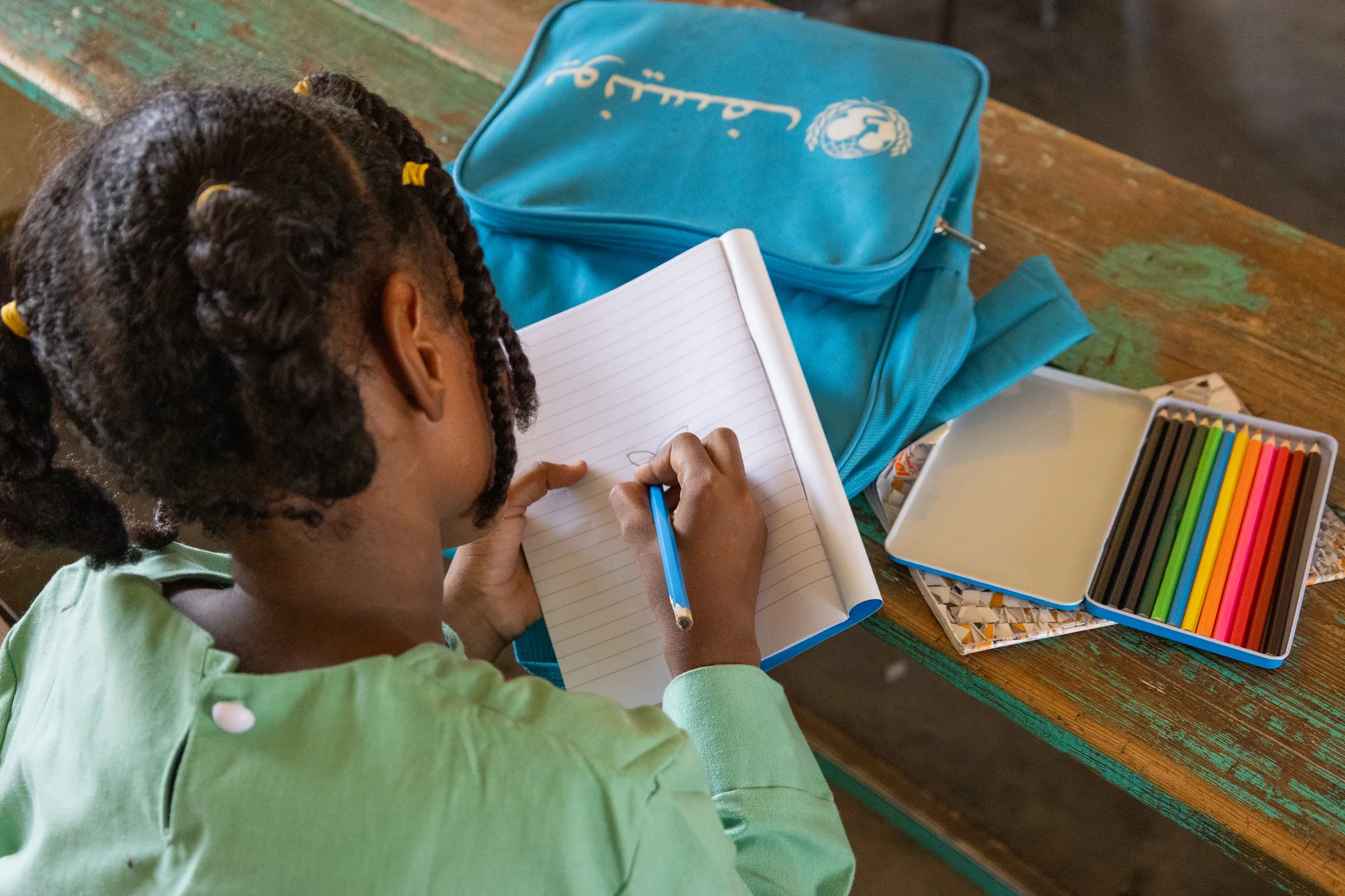 A young girl works in her classroom at Salalab Eastern Basic and Primary School in Port Sudan after fleeing conflict in Sinnar. With support from ECW and UNICEF, she received school supplies and a new uniform to help her continue learning.