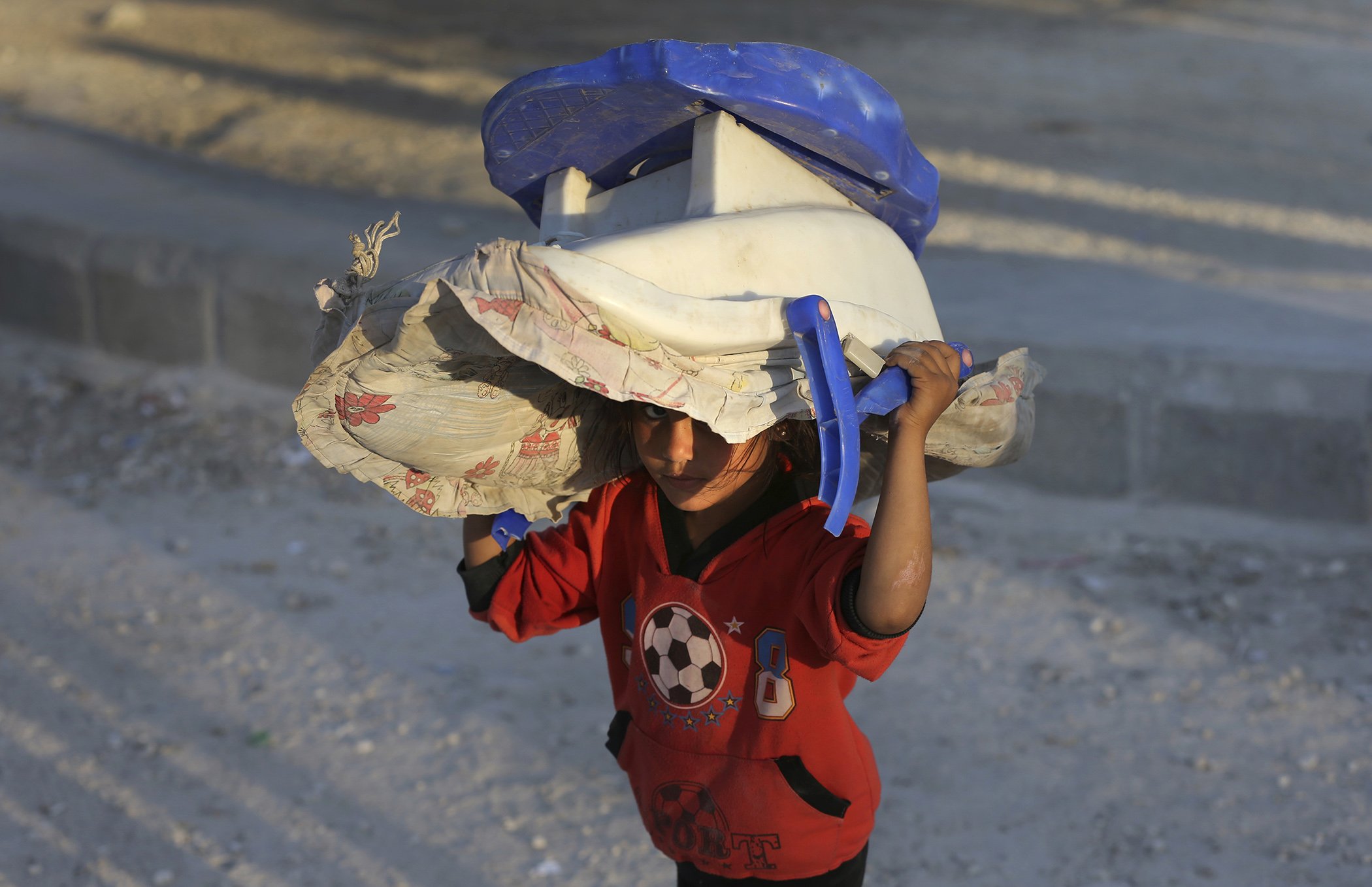 A Syrian displaced young girl who fled Raqqa city with her family carries a baby carseat on her head upon her arrival at a refugee camp, in Ain Issa town, northeast Syria, July 24, 2017.