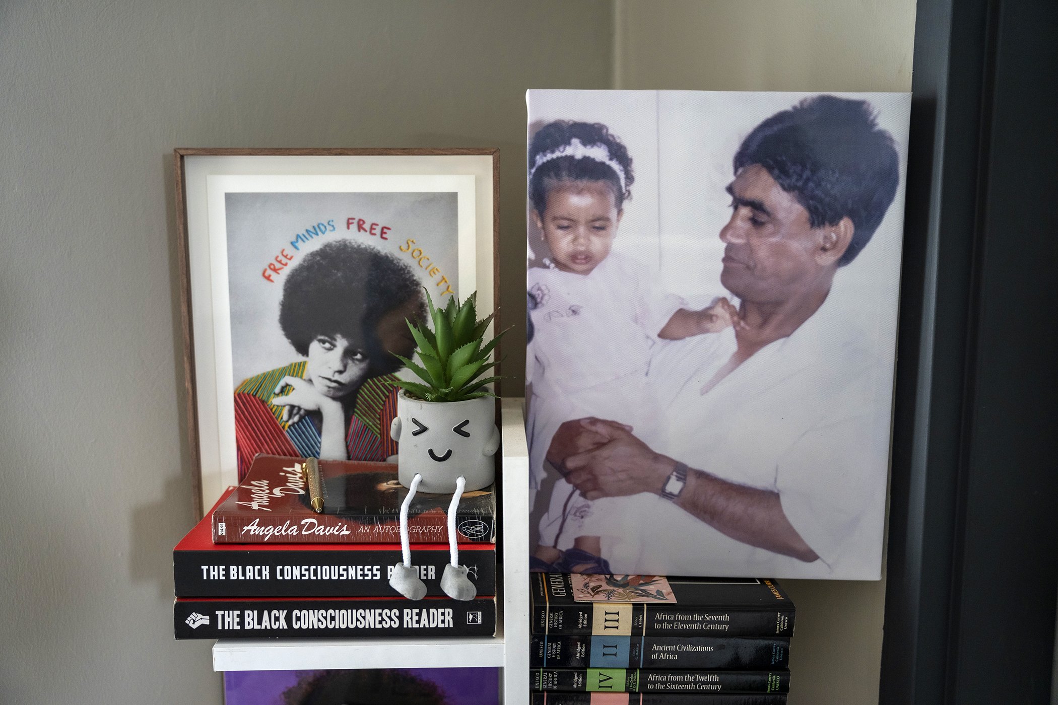 A bookshelf in the home of young activist Zulaikha Patel shows a poster of Angela Davis and another of a young Patel with her father.