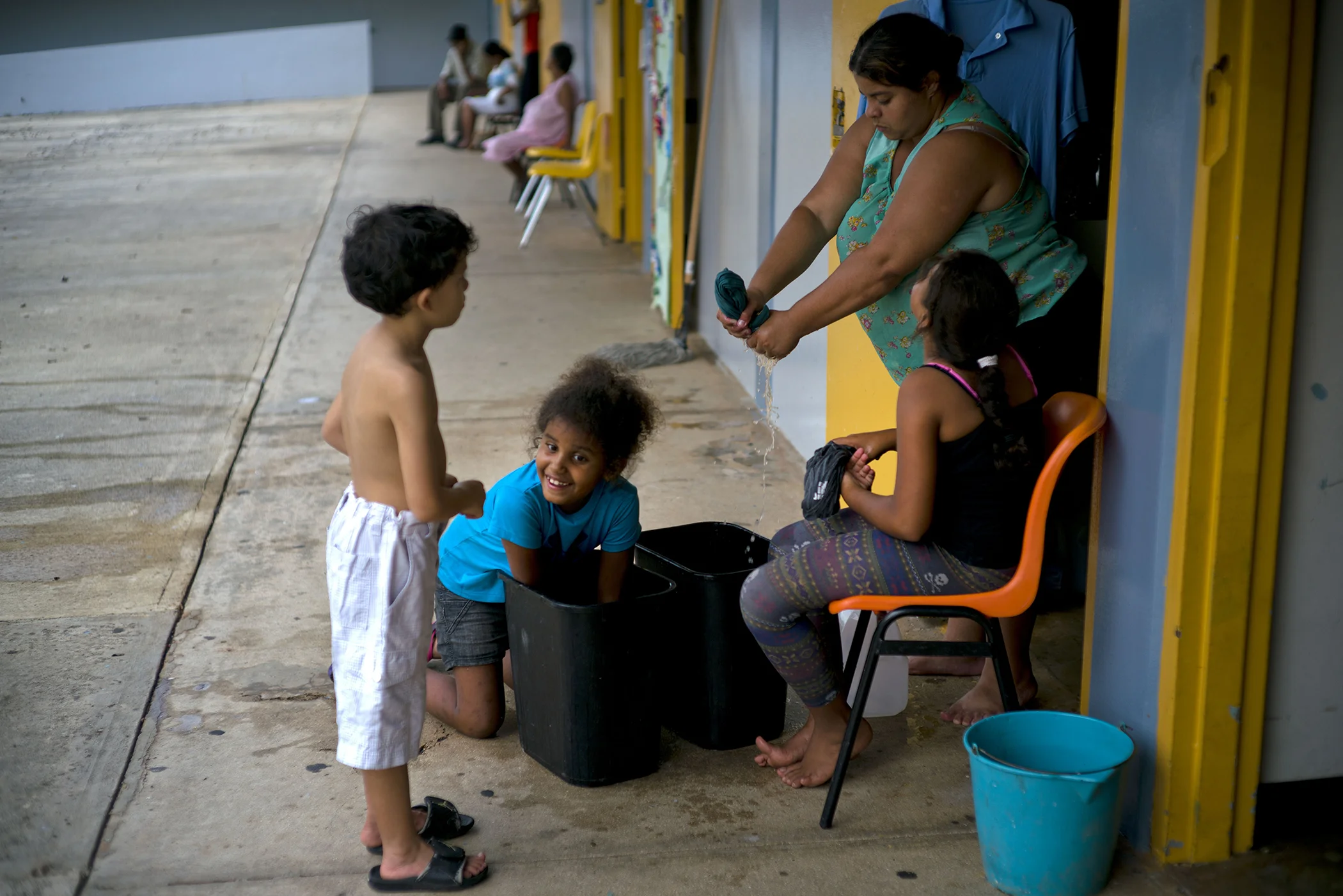 A woman rings out clothing in a plastic waste basket, as she washes clothes with the help of her daughters at a school-turned-shelter where their families were living after Hurricane Maria left them homeless in Toa Baja, Puerto Rico on Oct. 12, 2017.