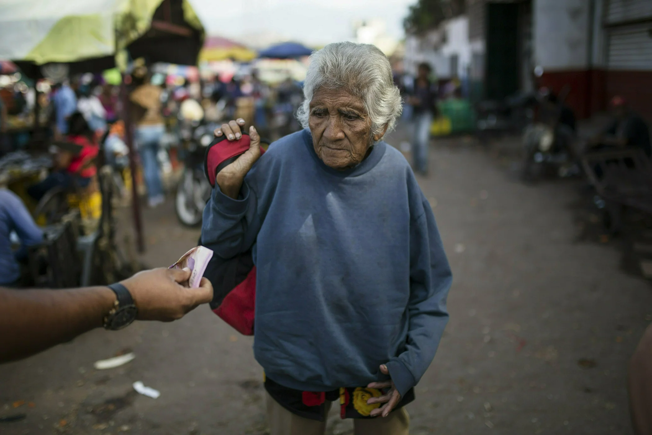 An elderly woman is offered cash as she begs at a wholesale food market in Caracas, Venezuela, Jan. 28, 2019.
